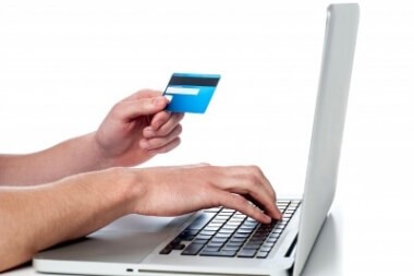Mans hand holding debit card and using laptop to get online.jpg